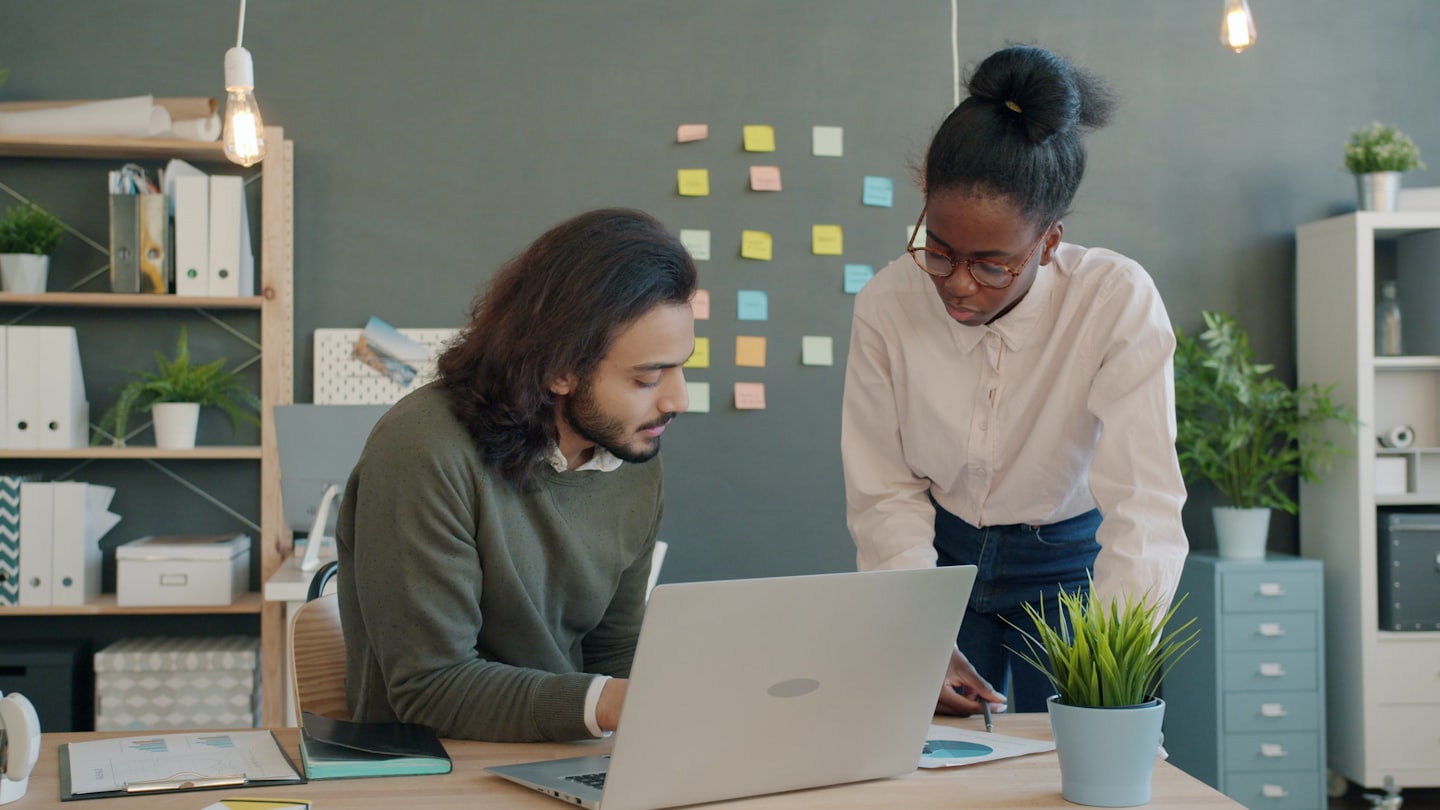 Two professionals collaborating over documents and laptop at a desk.